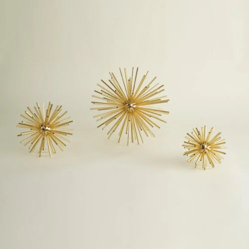 Three gold AUREOLE SCULPTURES of varying sizes are displayed against a plain, light background. Each features a spiky, metallic sunburst design that resembles abstract fireworks.