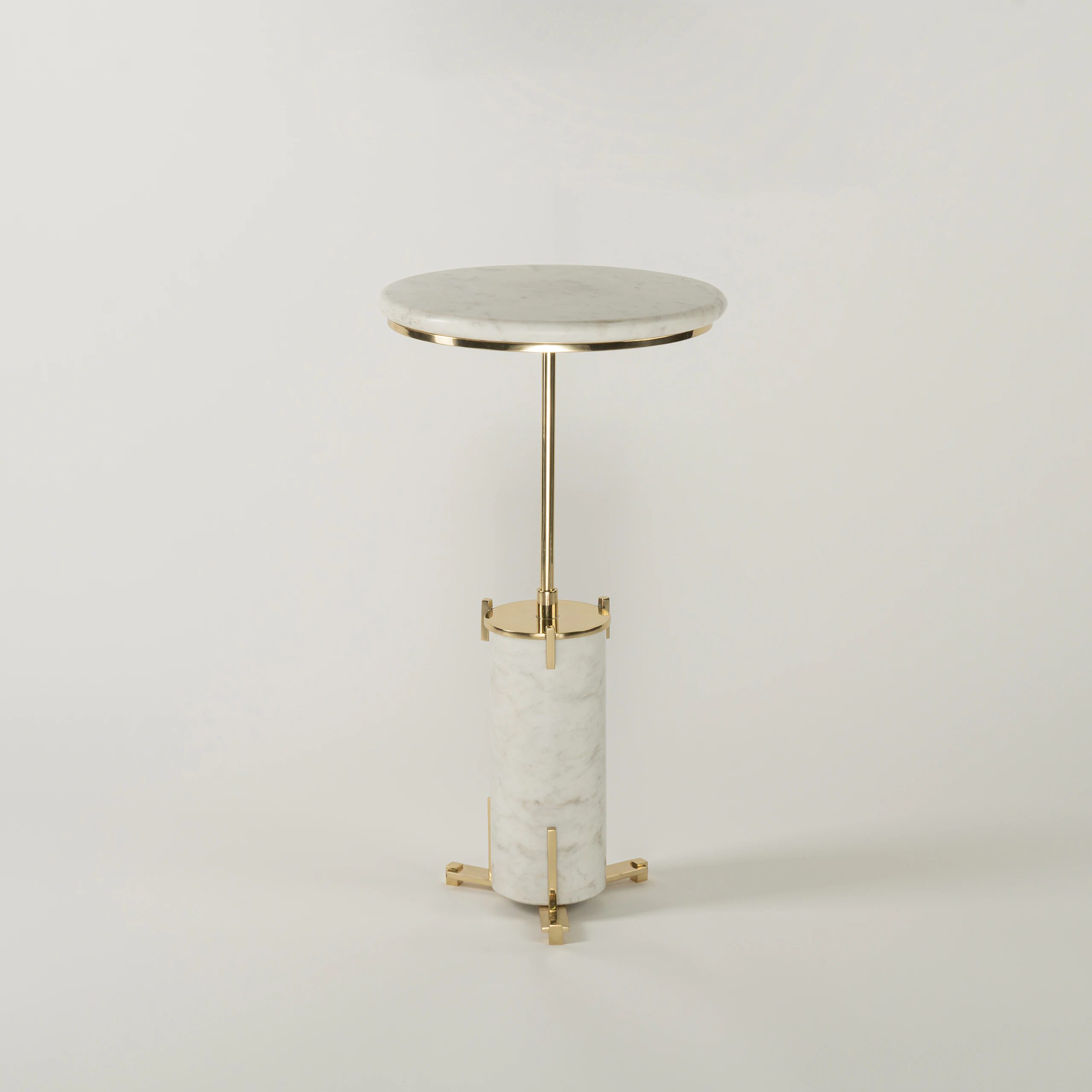 The HELIOS END TABLE features a round white marble top, slender gold metal stem, and cylindrical marble base with gold accents and three gold feet, shown against a plain white background. The HELIOS END TABLE features a round white marble top, slender gold metal stem, and cylindrical marble base with gold accents and three gold feet, shown against a plain white background.