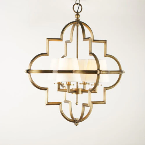 The QUATREFOIL PENDANT is a modern brass chandelier featuring a quatrefoil-shaped frame and six white fabric lampshades, shown suspended against a plain white background.