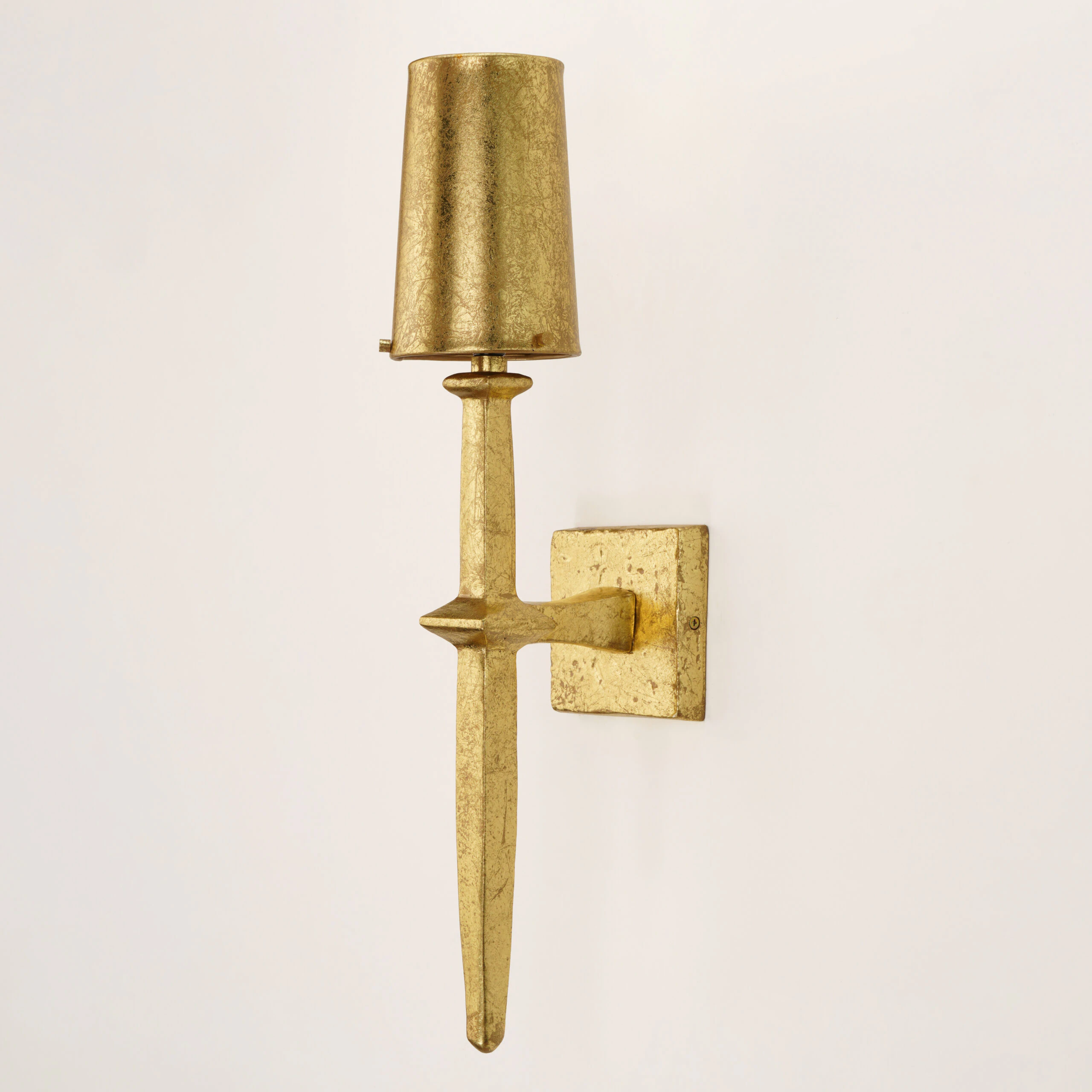 The ADAM WALL SCONCE features a gold textured finish, a tapered vertical base, and a matching cylindrical gold lampshade on a square wall plate, shown against a plain white background. The ADAM WALL SCONCE features a gold textured finish, a tapered vertical base, and a matching cylindrical gold lampshade on a square wall plate, shown against a plain white background.