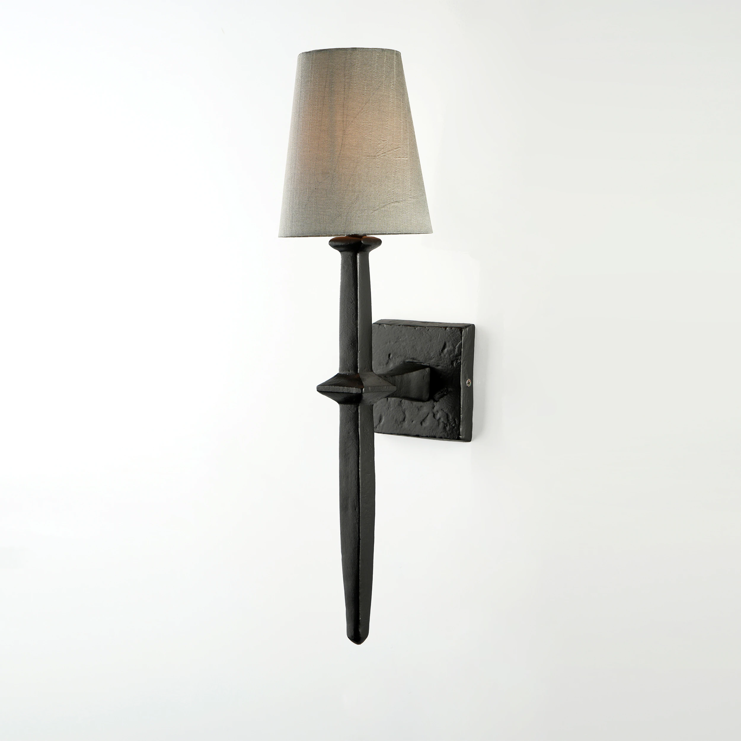 The ADAM WALL SCONCE features a black metal design with a textured square base, slim vertical body, and a light gray fabric lampshade, shown against a plain white background. The ADAM WALL SCONCE features a black metal design with a textured square base, slim vertical body, and a light gray fabric lampshade, shown against a plain white background.
