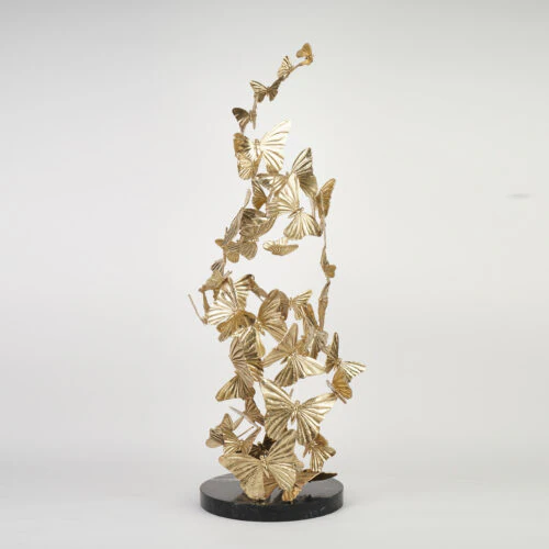 The CHRYSALIS SCULPTURE features gold metal butterflies in a swirling upward design, mounted on a round black base and displayed against a plain white background.