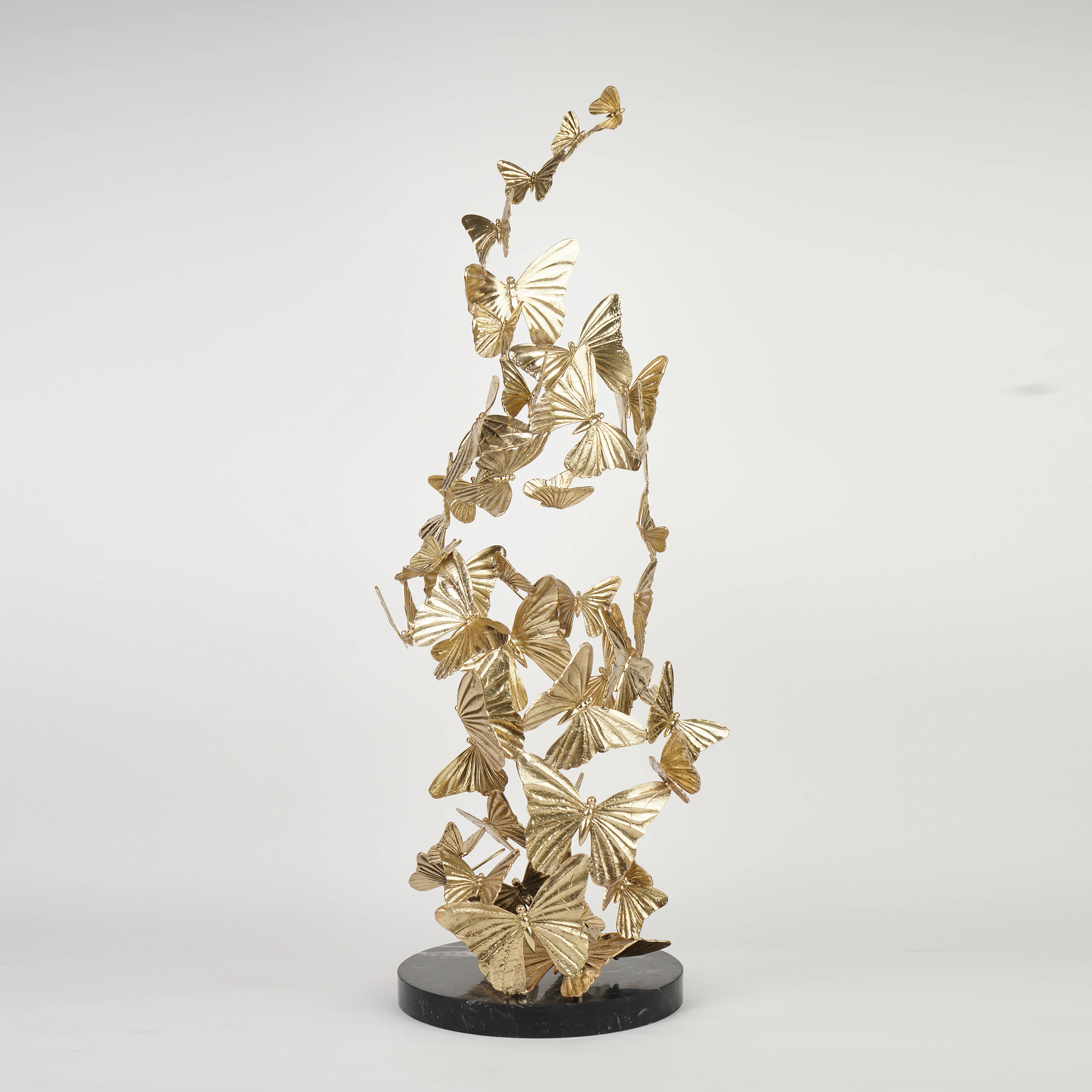 The CHRYSALIS SCULPTURE features gold metal butterflies in a swirling upward design, mounted on a round black base and displayed against a plain white background. The CHRYSALIS SCULPTURE features gold metal butterflies in a swirling upward design, mounted on a round black base and displayed against a plain white background.