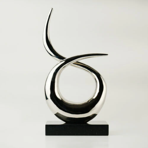 The VEGA SCULPTURE features two polished, curved metallic forms intertwined above a rectangular black base, displayed against a plain white background.