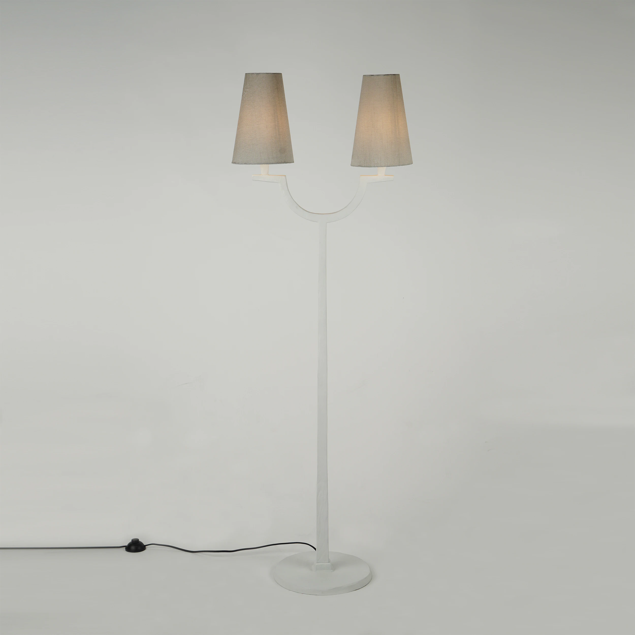 The MYKONOS FLOOR LAMP is a modern white floor lamp with two gray lampshades, a round base, and a black power cord with switch, shown against a plain light background. The MYKONOS FLOOR LAMP is a modern white floor lamp with two gray lampshades, a round base, and a black power cord with switch, shown against a plain light background.